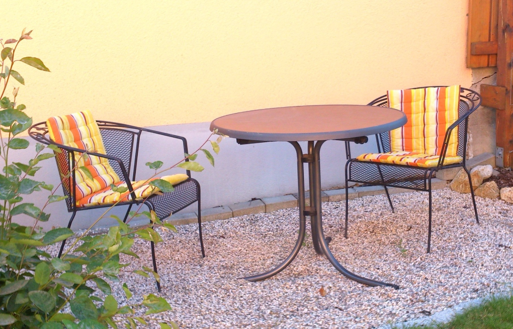 kleiner Gartentisch mit Stühlen vor oranger Hauswand